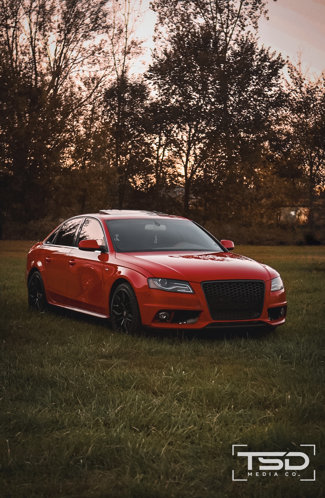 Red Audi sedan parked in an open field at sunset